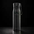 A matte black Hydra water bottle with a matching black flip-top lid and carrying loop, standing upright on a dark surface against a black background. The bottle features the HYDRA logo in white and a small blue accent, with 'FOUNDATION EDITION' printed near the bottom.