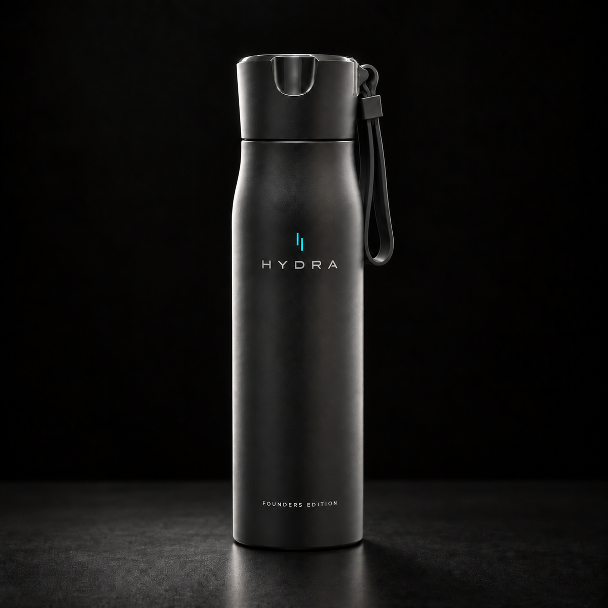 A matte black Hydra water bottle with a matching black flip-top lid and carrying loop, standing upright on a dark surface against a black background. The bottle features the HYDRA logo in white and a small blue accent, with 'FOUNDATION EDITION' printed near the bottom.
